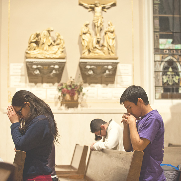 young adults with their heads bowed sitting in church pews praying
