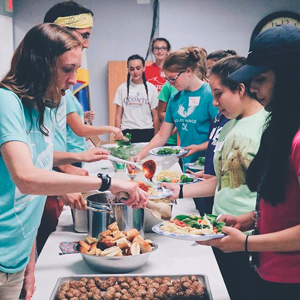 volunteers serving food to a group of you men and women