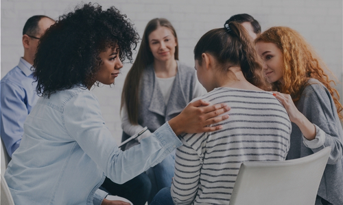 a group of people sit in a circle listening compassionately to a woman who is upset