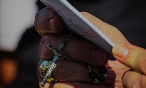 a closeup of a two hands holding a prayer card and rosary