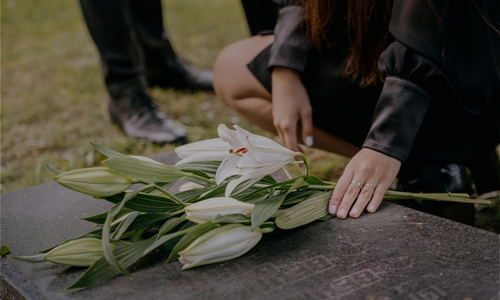 a person wearing black puts flowers down on a grave stone