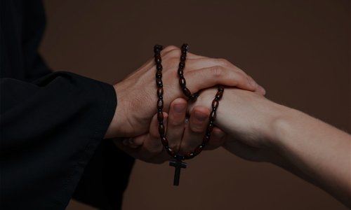 a priest holds the hand of a woman and there is a rosary wrapped around the hands