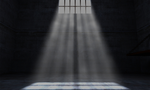 a dark and empty jail cell with light streaming in from between the bars of a small window