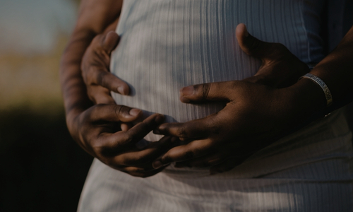 two people with hands wrapped around a pregnant woman's stomach