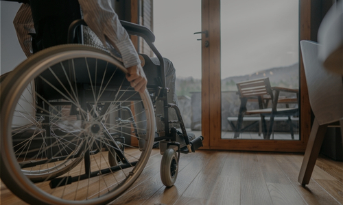 a person in a wheel chair looks out the glass doors at a hilly landscape